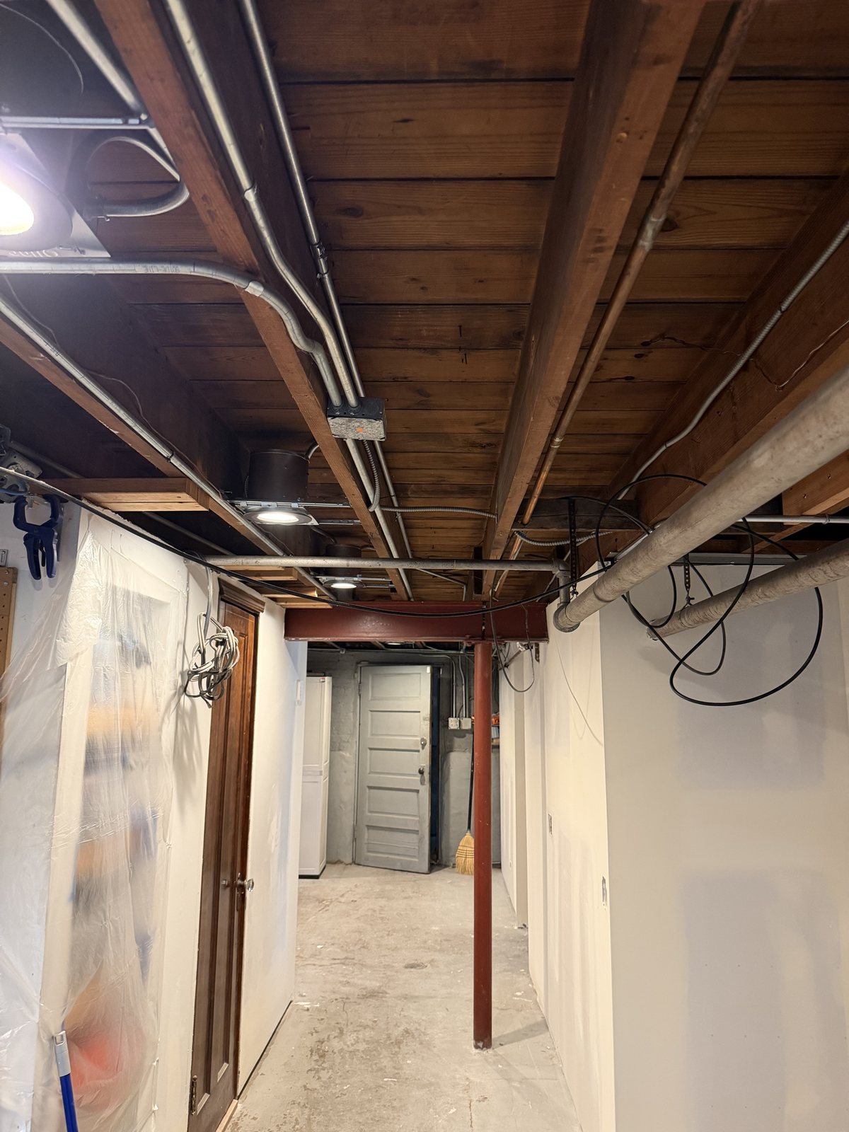 Basement with exposed bare wood joists, conduit and pipes before painting